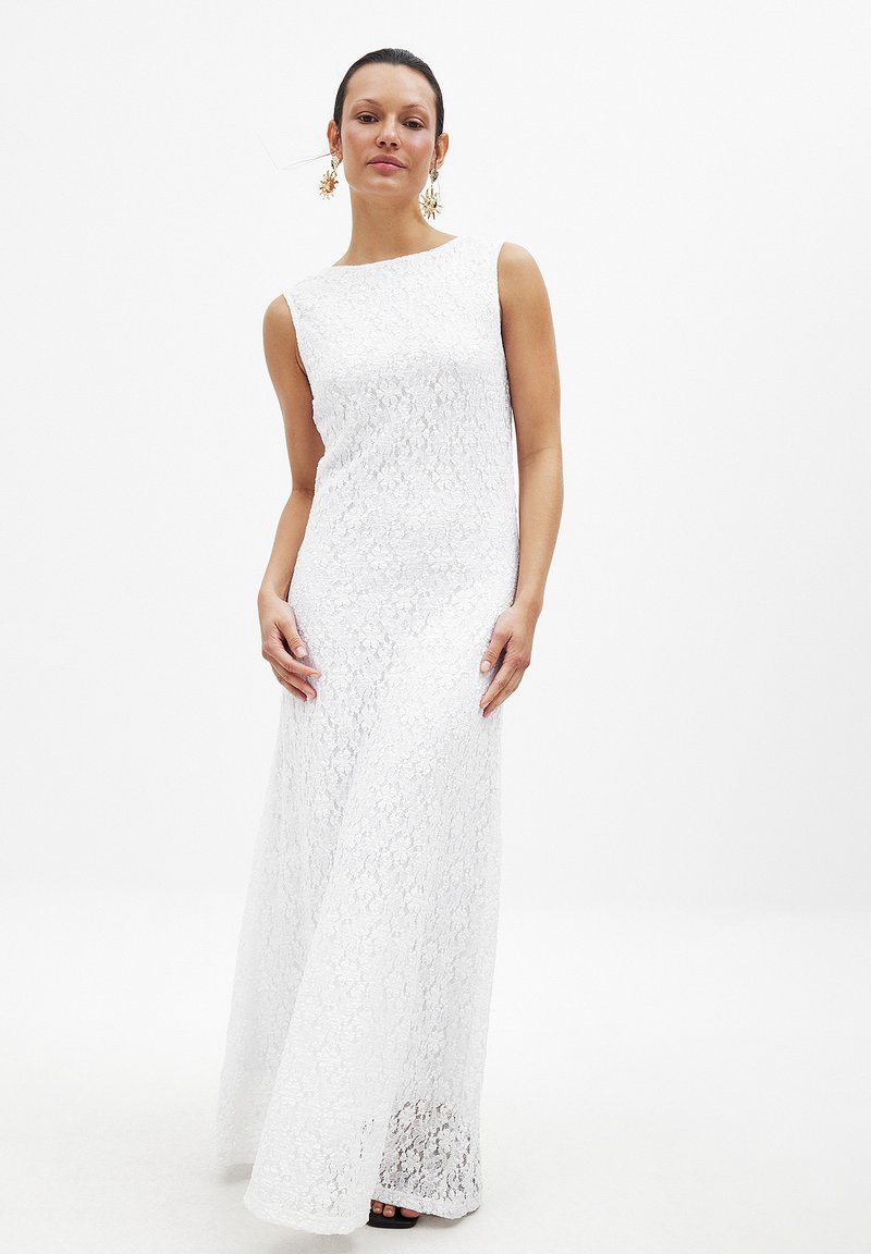 Witte kanten maxi-jurk met een mouwloos ontwerp, met een rechte silhoutte en ingewikkelde kanttextuur. Combinatie met zwarte schoenen.