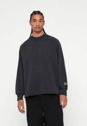 Tmavošedý sveter s kapucňou vyrobený z mäkkého materiálu, s rukávmi typu raglan, rebrovaným golierom a diskrétnym brandingom na prednej strane a na rukáve.