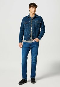 Dżinsowa kurtka w ciemnoniebieskim kolorze z dwoma kieszeniami na piersi, z zapięciem na guziki i luźnym krojem, w połączeniu z niebieskimi dżinsami i czarnymi butami.