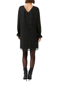 Czarna sukienka o fakturowanym splocie, z długimi, przejrzystymi rękawami, dekoltem w serek na plecach oraz koronkową lamówką na dole. W zestawieniu z czarnymi botkami za kostkę.