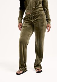 Oliwkowy aksamitny dres z krótką kurtką na suwak i spodniami z elastycznym pasem. Posiada boczne kieszenie na suwak oraz ozdobne przeszycia.