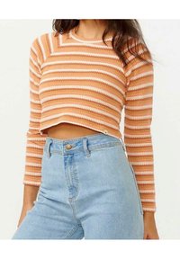 Striped cropped sweater i orange og hvid strik, med lange ærmer og ribbet tekstur, parret med højtaljede lyseblå jeans.