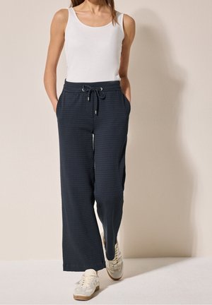 Pantalon large texturé bleu marine avec taille élastique et cordon de serrage. Style avec un débardeur blanc et des baskets de couleur claire.