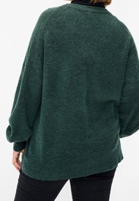 Grüner übergroßer Pullover mit strukturierter Strickmusterung, gerippten Bündchen und abgerundetem Saum. Leichter Stoff, lockere Passform, sichtbare Nahtdetails am Rücken.