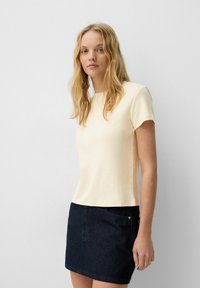 Lichtgele t-shirt met korte mouwen en een ronde hals, met een gladde textuur en een aansluitend ontwerp, gecombineerd met een donkerdenimrok met een knoop.
