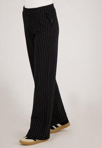 Zwart gestreepte broek met een losse pasvorm, voorzien van een wijde pijp, elastische tailleband en zijzakken. Het materiaal lijkt textuur te hebben.