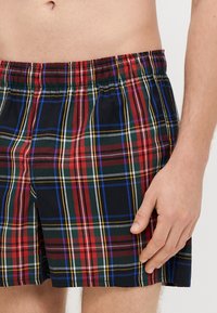 Kąpielówki w kratę, z czerwonym, zielonym, czarnym i żółtym wzorem, posiadają elastyczny pas i luźny fason, wykonane z lekkiego materiału.