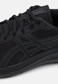 Black athletic shoe with mesh upper, textured detailing, and tonal logo. Features laces for closure and a durable rubber sole design.