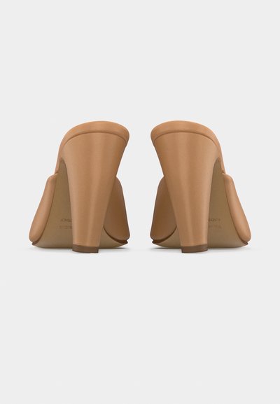 Mules à talons hauts de couleur beige, vue de dos, avec des talons larges et carrés et une finition en cuir lisse sur fond blanc.