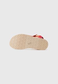 Rubber sandal sole with a textured, geometric pattern in light beige, featuring bright pink straps and a branded logo near the heel.
