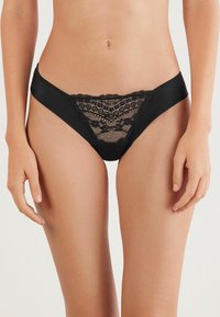 Tanga de encaje negro y satén con intrincados detalles de encaje en la parte frontal, lados suaves y un corte de cintura baja. Textura suave, diseño delicado.