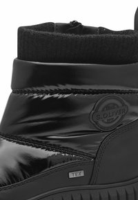 Bottines noires avec une finition en vernis brillant, un revers en tricot, une semelle texturée et un détail de logo en relief, avec une étiquette "TEX" sur le côté.