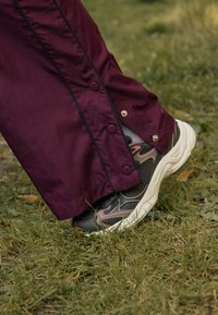 Maroon tuulihaalari, jossa on nepparit, yhdistettynä mustiin ja beigeihin kuvioituihin lenkkareihin, joissa on paksu valkoinen pohja, lepäämässä nurmikolla.