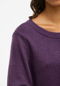 Lilla strikkegenser med ribbestrikket halslinning, myk tekstur og drop shoulders, som viser et subtilt, jevnt vevemønster.