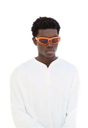 Occhiali da sole arancioni con montatura spessa e lenti colorate, indossati con una camicia bianca a maniche lunghe con scollatura tipo henley.