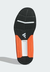 Suela de zapato de goma negra con acentos en naranja y blanco. Presenta una superficie texturizada, un patrón de relieve distintivo y una sección etiquetada.