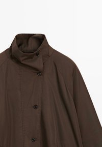 Manteau marron foncé à col montant avec fermeture asymétrique à boutons et manches longues, présenté sur un fond blanc uni.