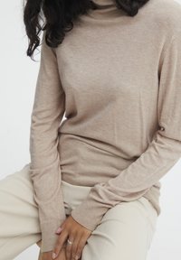 Maglione a collo alto beige realizzato in materiale morbido e leggero; presenta maniche lunghe e orlo a coste, abbinato a pantaloni crema.