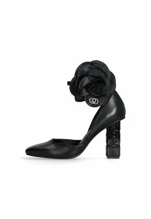 Chaussure à talon haut en cuir noir avec talon carré présentant un motif embossé et un grand détail en tissu en forme de rose avec un logo métallique sur la sangle de la cheville.
