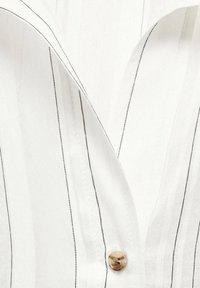 Witte shirt met dunne zwarte strepen, met een kraaghalslijn en een ronde, doorzichtige knop bij de knoopsluiting. Glad textuur.