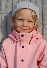 Vedenkestävä vaaleanpunainen takki korkealla kauluksella, mustat nappikiinnitykset ja harmaa ribbikuvioinen myssy. Sujuva pinta ja moderni muotoilu.