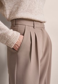 Beige wool sweater and light brown pleated trousers with side pockets and a tailored fit, highlighting soft textures and clean lines.