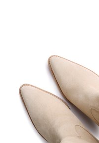 Botas de tobillo de ante beige con punta afilada, detalles de costura a lo largo de la suela y textura suave. Diseño minimalista sin herrajes visibles.