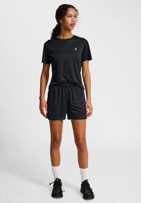 Svart atletisk outfit bestående av en kortärmad topp och shorts, tillverkad av ett glatt, lättviktigt material, med ett elastiskt midjeband och logodetalj.