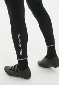 Svarta cykelbyxor med reflexdetaljer och logotypen "ENDURANCE" i vitt. I kombination med eleganta svarta cykelskor.