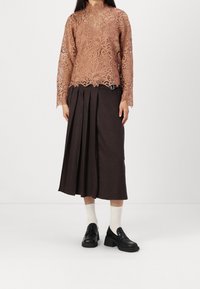 Haut à manches longues en dentelle rose poudré avec motifs floraux ; jupe midi plissée taille haute marron ; mocassins noirs épais et chaussettes blanches.