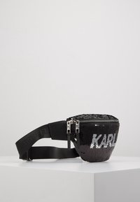 Marsupio nero con paillettes, dalla forma arrotondata, con un compartimento principale con zip, cintura regolabile e logo "KARL" in argento.