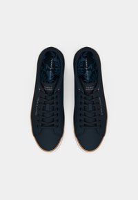 Et par marineblå Tommy Hilfiger sneakers med snørebånd, hvide såler og mærkede indlægssåler med bladmønstre, set fra oven.