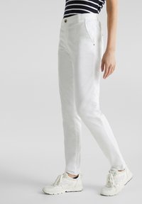 Pantalon blanc à coupe classique, fabriqué en tissu lisse. Doté d'une fermeture par bouton, de poches latérales, porté avec des baskets blanches.