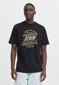 Černé bavlněné tričko s velkým grafikou v zlaté a bílé barvě s nápisem "DENIM AUTHENTIC IN STYLE" a kulatým výstřihem a krátkými rukávy.