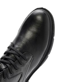 Zapato de cuero negro con acabado texturizado, punta redondeada, diseño de cordones y suela de goma. Detalles de costura a lo largo del borde.
