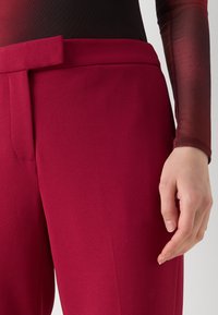Rode op maat gemaakte broek met een gladde textuur en een hoge taille, voorzien van een vlakke voorkant en een zijzak, gecombineerd met een getailleerde zwarte top.