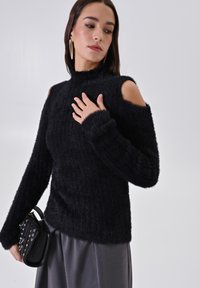 Maglione nero in maglia fuzzy con colletto alto e design con spalle scoperte. Texture a coste, maniche lunghe e silhouette aderente.
