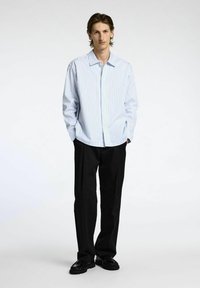 En ljusblå och vit randig skjorta med knappar för män, i kombination med svarta byxor och skor. Skjortan har en avslappnad passform och långa ärmar.