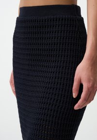 Jupe tricotée bleu marine avec un motif texturé, taille haute et silhouette ajustée, révélant une doublure subtile.