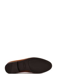 Zapato de ante marrón con punta redonda, suela de goma oscura texturizada y un ribete de cuero liso, que presenta un detallado pespunte en los bordes.