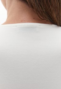 Primer plano de la parte superior de la espalda y el cuello de una persona con cabello castaño claro y vistiendo una camisa blanca sencilla.