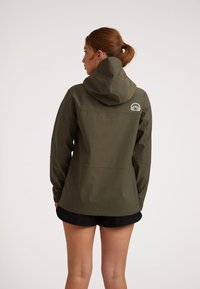 Giacca impermeabile verde oliva con cappuccio, design senza particolari, un logo sul retro e una texture liscia. Indossata con pantaloni corti neri.