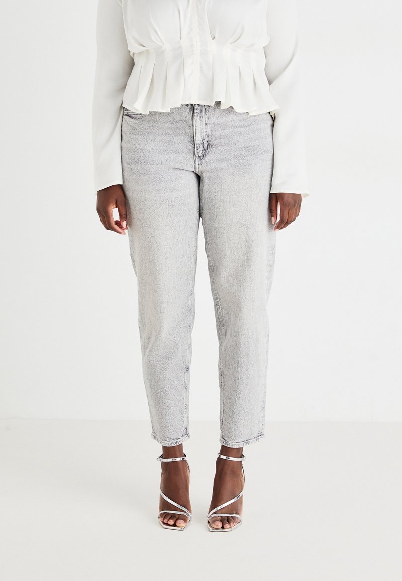 Jeans de mezclilla gris claro con un corte recto, que presentan una textura desgastada. Combinados con una blusa blanca con volantes y sandalias de tacón plateadas.