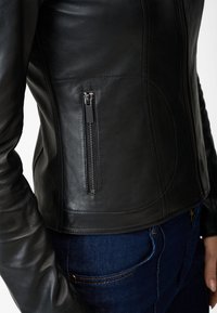 Schwarze Lederjacke mit tailliertem Schnitt, ausgestattet mit einer seitlichen Reißverschlusstasche, glatter Textur und subtilen Nähten.