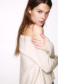 Beige off-shoulder sweater with a textured knit. The fabric appears soft, featuring a relaxed fit with a slight drape.