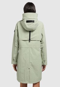 Parka de culoare verde deschis, până la genunchi, cu glugă ajustabilă, fermoar frontal și buzunar cu clapetă. Material texturat cu detalii cusute pe cusături.