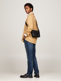 Borsa a tracolla nera con superficie texture, indossata sopra una camicia button-up beige, abbinata a jeans blu e mocassini neri.