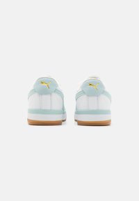 White sneakers with light blue accents, textured leather, and rubber soles. Features a gold logo at the heel and padded collar for support.