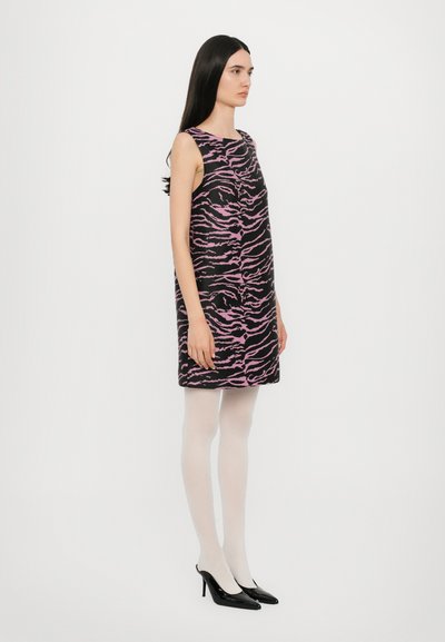 Schwarzes ärmelloses Kleid mit rosa Tigermuster, gerade geschnitten, aus strukturiertem Stoff, kombiniert mit weißen Strumpfhosen und schwarzen High Heels.