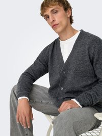 Dark gray cardigan with ribbed texture, V-neck, and five buttons, worn over a white henley shirt, paired with light gray jeans.